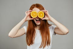 Glückliches junges Mädchen, das zwei Scheiben Orange an ihrem Gesicht über grauem Hintergrund hält stockfotografie Glückliches junges Mädchen, das zwei Scheiben Orange an ihrem Gesicht über grauem Hintergrund hält stockfotografie