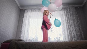 Glückliches kleines Mädchen, das nahe dem Fenster auf dem Bett in der Kindertagesstätte mit dem Bündel von Luftballonen in ihren stock video Glückliches kleines Mädchen, das nahe dem Fenster auf dem Bett in der Kindertagesstätte mit dem Bündel von Luftballonen in ihren stock video
