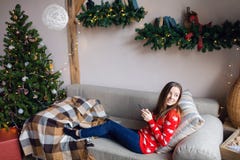 Glückliches Mädchen, das Inhalt auf Linie in einem intelligenten Telefon strömend zu Hause sitzt auf einem Sofa im Winter aufpass lizenzfreie stockfotos Glückliches Mädchen, das Inhalt auf Linie in einem intelligenten Telefon strömend zu Hause sitzt auf einem Sofa im Winter aufpass lizenzfreie stockfotos