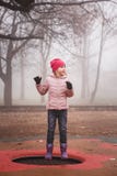 Glückliches Mädchen in einer rosa Jacke, die draußen auf die Trampoline in Park springt Herbst, nebelhafter Wald lizenzfreies stockfoto Glückliches Mädchen in einer rosa Jacke, die draußen auf die Trampoline in Park springt Herbst, nebelhafter Wald lizenzfreies stockfoto