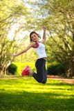 Glückliches sportives Mädchen, das in grünen Sommerpark springt lizenzfreie stockbilder Glückliches sportives Mädchen, das in grünen Sommerpark springt lizenzfreie stockbilder