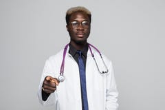 Gniewnej afrykańskiej czarnej samiec doktorski wskazuje palec przy tobą z stetoskopem wokoło jego szyi na szarość obrazy stock Gniewnej afrykańskiej czarnej samiec doktorski wskazuje palec przy tobą z stetoskopem wokoło jego szyi na szarość obrazy stock