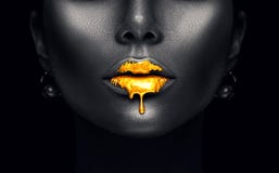 Gold paint drips from the lips, golden liquid drops on beautiful model girl`s mouth, creative abstract dark black skin makeup
