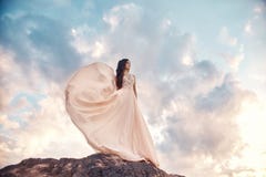 Gorgeous woman brunette in the mountains at sunset and blue sky with clouds. The woman looks into the distance in a long white royalty free stock photos Gorgeous woman brunette in the mountains at sunset and blue sky with clouds. The woman looks into the distance in a long white royalty free stock photos