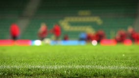 A grama do campo de futebol com chuva deixa cair com processo unfocused do treinamento da equipe no fundo A grama do campo de futebol com chuva deixa cair com processo unfocused do treinamento da equipe no fundo