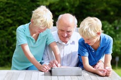 Grandkids che insegnano al nonno ad utilizzare il pc della compressa immagini stock Grandkids che insegnano al nonno ad utilizzare il pc della compressa immagini stock