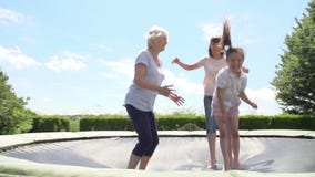 Grandmother, Granddaughter And Mother Bouncing On Trampoline