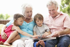 Grandparents And Grandchildren Reading Book On Garden Seat stock photo Grandparents And Grandchildren Reading Book On Garden Seat stock photo