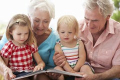 Grandparents And Grandchildren Reading Book On Garden Seat royalty free stock image Grandparents And Grandchildren Reading Book On Garden Seat royalty free stock image