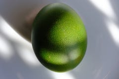 Green Easter egg on a white platter. A ray of sun shining on the egg. High resolution closeup macro royalty free stock image Green Easter egg on a white platter. A ray of sun shining on the egg. High resolution closeup macro royalty free stock image