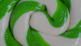 Green and white large spiral candy lollipop on rotating surface - close up