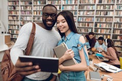 Groep etnische multiculturele studenten in bibliotheek De zwarte kerel en het asial meisje gebruiken tablet royalty-vrije stock foto's Groep etnische multiculturele studenten in bibliotheek De zwarte kerel en het asial meisje gebruiken tablet royalty-vrije stock foto's
