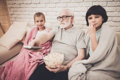 Grootvader, kleinzoon en kleindochter thuis De opa en de kinderen letten op film op TV en eten popcorn stock foto Grootvader, kleinzoon en kleindochter thuis De opa en de kinderen letten op film op TV en eten popcorn stock foto