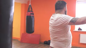 Gros homme barbu fatigué de la boxe s'exerçante un sac de sable dans le gymnase, sport Gros homme barbu fatigué de la boxe s'exerçante un sac de sable dans le gymnase, sport
