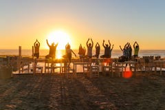 Group doing yoga exercises the beach at sunset