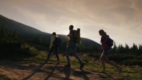 A group of friends with backpacks rises up the mountain. In the rays of the setting sun. Active lifestyle