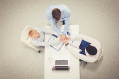 Group of happy business people holding hands together while sitting around the desk stock photo Group of happy business people holding hands together while sitting around the desk stock photo