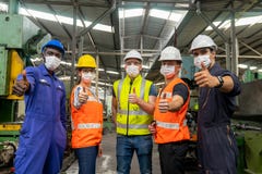 Group of multiethnic engineer with workers giving thumbs up and  wearing surgical mask to prevent covid-19 in manufacturing