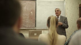 Group of students in a classroom, listening as their teacher holds a lecture stock video Group of students in a classroom, listening as their teacher holds a lecture stock video