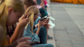 Group of teenagers sitting on street and using smartphones