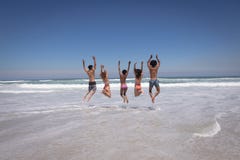 Groupe heureux d'amis sautant ensemble sur la plage au soleil image stock Groupe heureux d'amis sautant ensemble sur la plage au soleil image stock