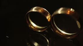 Großaufnahme der goldenen Eheringe, die auf dem dunklen Hintergrund liegen Lichtstrahlen belichten die Ringe stock video footage Großaufnahme der goldenen Eheringe, die auf dem dunklen Hintergrund liegen Lichtstrahlen belichten die Ringe stock video footage