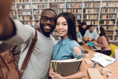Grupa etniczni wielokulturowi ucznie w bibliotece Czarnego faceta i azjata dziewczyna bierze selfie na telefonie zdjęcia stock Grupa etniczni wielokulturowi ucznie w bibliotece Czarnego faceta i azjata dziewczyna bierze selfie na telefonie zdjęcia stock