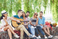 Grupo de amigos felices con la guitarra Mientras que uno de ellos está tocando la guitarra y otros le están dando un aplauso foto de archivo libre de regalías Grupo de amigos felices con la guitarra Mientras que uno de ellos está tocando la guitarra y otros le están dando un aplauso foto de archivo libre de regalías