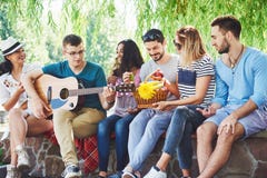 Grupo de amigos felices con la guitarra Mientras que uno de ellos está tocando la guitarra y otros le están dando un aplauso fotografía de archivo Grupo de amigos felices con la guitarra Mientras que uno de ellos está tocando la guitarra y otros le están dando un aplauso fotografía de archivo