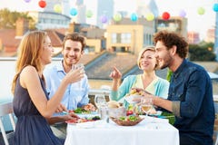 Grupo de amigos que comem a refeição no terraço do telhado imagens de stock Grupo de amigos que comem a refeição no terraço do telhado imagens de stock