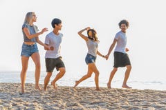 Grupo de amigos que têm o divertimento que corre abaixo da praia no por do sol foto de stock royalty free Grupo de amigos que têm o divertimento que corre abaixo da praia no por do sol foto de stock royalty free