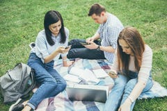 Grupo de estudiantes universitarios que se sientan al aire libre usando los teléfonos móviles fotografía de archivo Grupo de estudiantes universitarios que se sientan al aire libre usando los teléfonos móviles fotografía de archivo