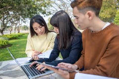 Grupo de sentada asi?tica de los estudiantes universitarios en el funcionamiento de la hierba verde y de lectura afuera junto en foto de archivo Grupo de sentada asi?tica de los estudiantes universitarios en el funcionamiento de la hierba verde y de lectura afuera junto en foto de archivo