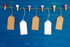 Grupo dos preços ou de etiquetas do papel vazio e pinos de madeira decorados nos corações coloridos que penduram em uma corda no Fotos de Stock Grupo dos preços ou de etiquetas do papel vazio e pinos de madeira decorados nos corações coloridos que penduram em uma corda no Fotos de Stock