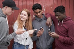 Grupp av ton?rs- v?nner som ser mobiltelefoner i stads- inst?llning royaltyfria foton Grupp av ton?rs- v?nner som ser mobiltelefoner i stads- inst?llning royaltyfria foton