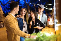Gruppen av attraktiva unga vänner som talar och besöker, äter marknaden i gatan royaltyfri fotografi Gruppen av attraktiva unga vänner som talar och besöker, äter marknaden i gatan royaltyfri fotografi