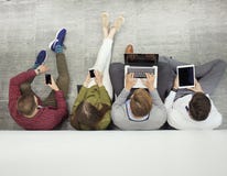 Gruppo di giovani attraenti che si siedono sul pavimento facendo uso di un computer portatile, PC della compressa, Smart Phone, s fotografia stock Gruppo di giovani attraenti che si siedono sul pavimento facendo uso di un computer portatile, PC della compressa, Smart Phone, s fotografia stock