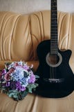 A guitarra e o ramalhete estão em um sofá de couro imagens de stock royalty free A guitarra e o ramalhete estão em um sofá de couro imagens de stock royalty free