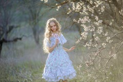 Gullig flicka f?r blont h?r i en l?ng winded kl?nning som g?r, i att blomma frukttr?dg?rden fotografering för bildbyråer Gullig flicka f?r blont h?r i en l?ng winded kl?nning som g?r, i att blomma frukttr?dg?rden fotografering för bildbyråer