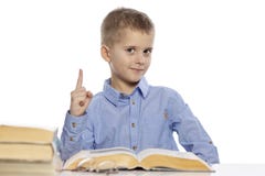 Gullig le skolpojke som sitter på tabellen med kurser Han lyftte upp hans finger bakgrund isolerad white royaltyfria bilder Gullig le skolpojke som sitter på tabellen med kurser Han lyftte upp hans finger bakgrund isolerad white royaltyfria bilder