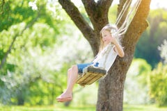 Gullig liten flicka som har gyckel på en gunga, i att blomstra den gamla trädgården för äppleträd utomhus på solig vårdag arkivfoton Gullig liten flicka som har gyckel på en gunga, i att blomstra den gamla trädgården för äppleträd utomhus på solig vårdag arkivfoton