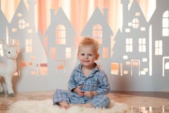 Gullig pys för blont hår i sleepwear nära hus för julleksakpapper arkivbild Gullig pys för blont hår i sleepwear nära hus för julleksakpapper arkivbild