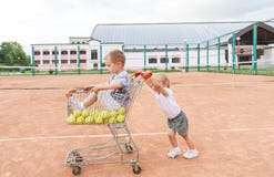 Gulliga barn som spelar på tennisbanan Pys- och tennisbollar i den shoppa vagnen royaltyfria bilder Gulliga barn som spelar på tennisbanan Pys- och tennisbollar i den shoppa vagnen royaltyfria bilder
