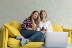 H?rlig lesbisk kvinna som tv? ?r kvinnlig i tillf?llig kl?der som tillsammans hemma sitter p? den gula soffan arkivfoto H?rlig lesbisk kvinna som tv? ?r kvinnlig i tillf?llig kl?der som tillsammans hemma sitter p? den gula soffan arkivfoto