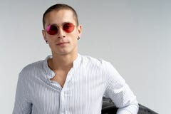 Halv l?ngdst?ende av den h?rliga unga mannen i r?d solglas?gon, b?rande vit skjorta som lutas p? det stora gummihjulet som ?ver i royaltyfri foto Halv l?ngdst?ende av den h?rliga unga mannen i r?d solglas?gon, b?rande vit skjorta som lutas p? det stora gummihjulet som ?ver i royaltyfri foto