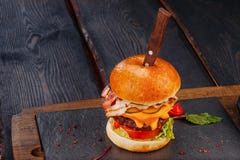 Hamburger juteux avec du fromage de jambon, de boeuf et de cheddar sur le conseil en bois rustique avec le couteau images libres de droits Hamburger juteux avec du fromage de jambon, de boeuf et de cheddar sur le conseil en bois rustique avec le couteau images libres de droits