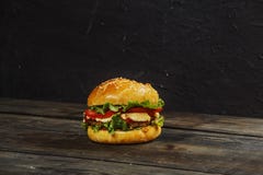 Hamburger on a wooden board against a dark background with copy space. Hamburger with sauce and fresh vegetables on a wooden table royalty free stock images Hamburger on a wooden board against a dark background with copy space. Hamburger with sauce and fresh vegetables on a wooden table royalty free stock images