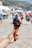 Hand die donker chocoladeroomijs in wafelkegel houden over de vage achtergrond van de straatstad royalty-vrije stock afbeelding Hand die donker chocoladeroomijs in wafelkegel houden over de vage achtergrond van de straatstad royalty-vrije stock afbeelding