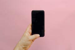 Hand die modieuze zwarte telefoon met het lege scherm op roze backg houden royalty-vrije stock afbeeldingen Hand die modieuze zwarte telefoon met het lege scherm op roze backg houden royalty-vrije stock afbeeldingen