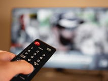 Hand holding remote control in front of television stock photo Hand holding remote control in front of television stock photo